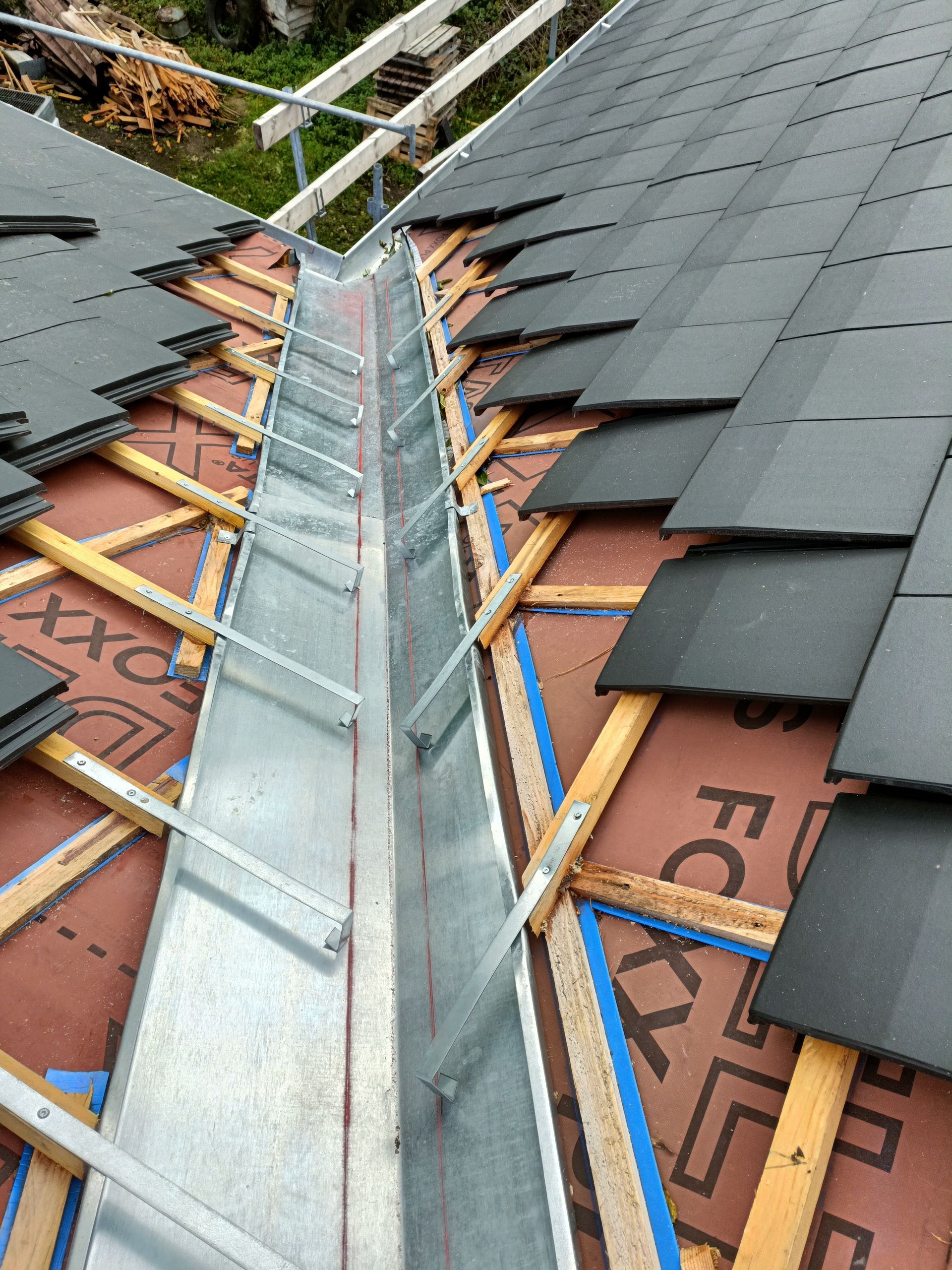 Noue de toit avec solins métalliques et bardeaux foncés, laissant apparaître la sous-couche des deux côtés.