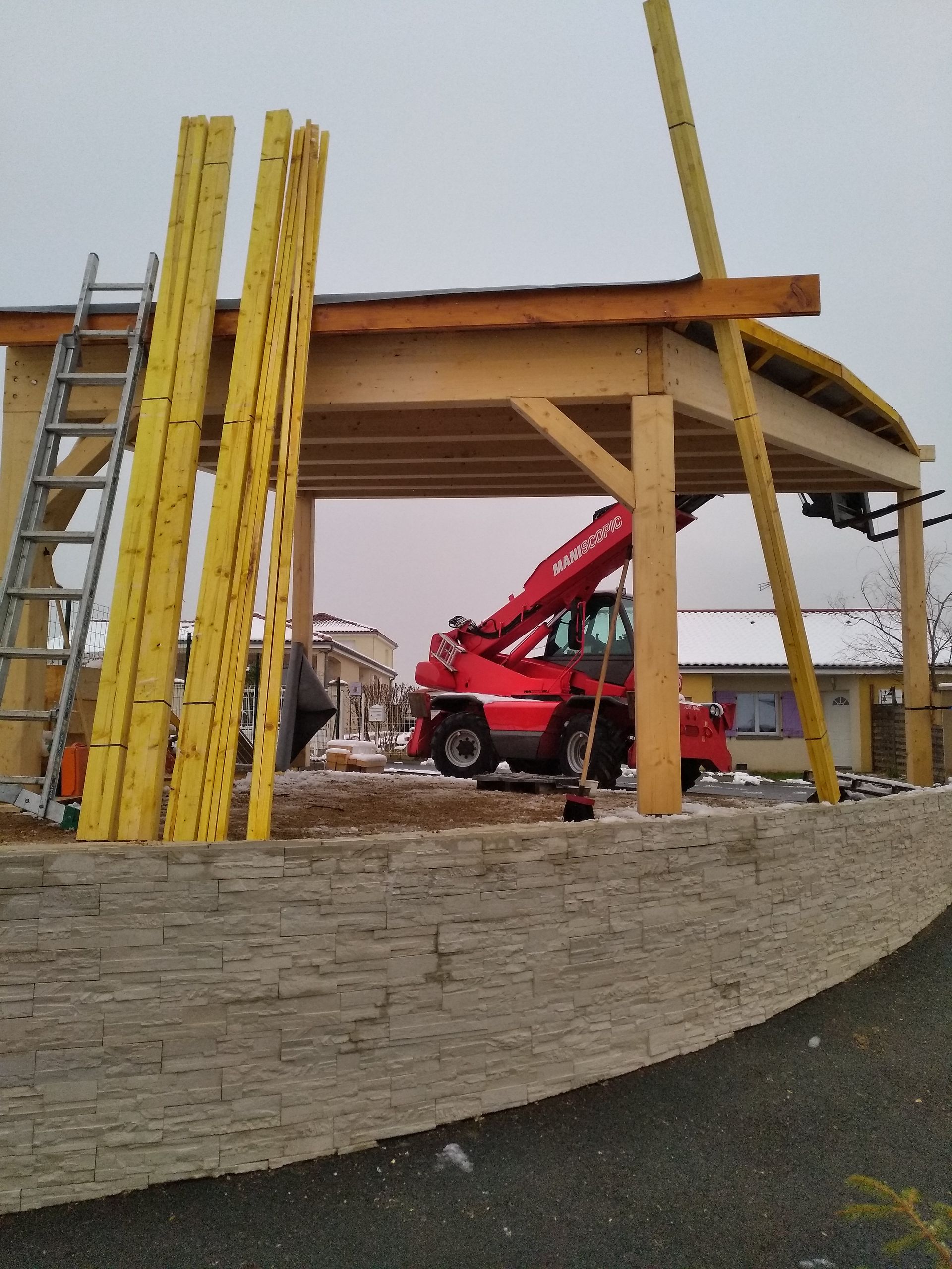 Chantier de construction avec échafaudages jaunes, camion-grue rouge et structure couverte sur un terrain vague.