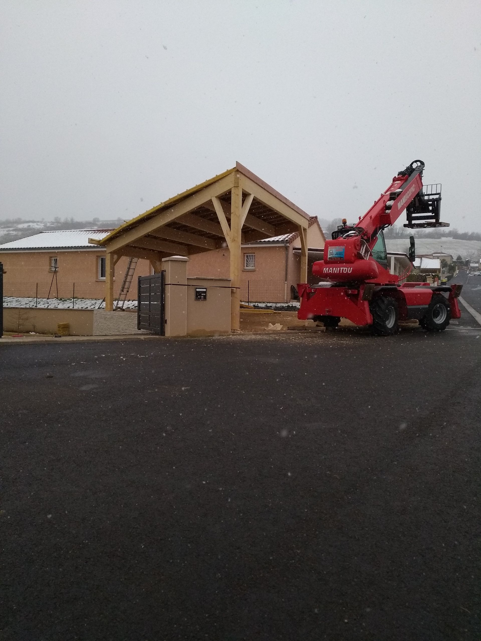 Rue enneigée avec un bâtiment en bois et un camion-nacelle élévateur rouge garé à côté.