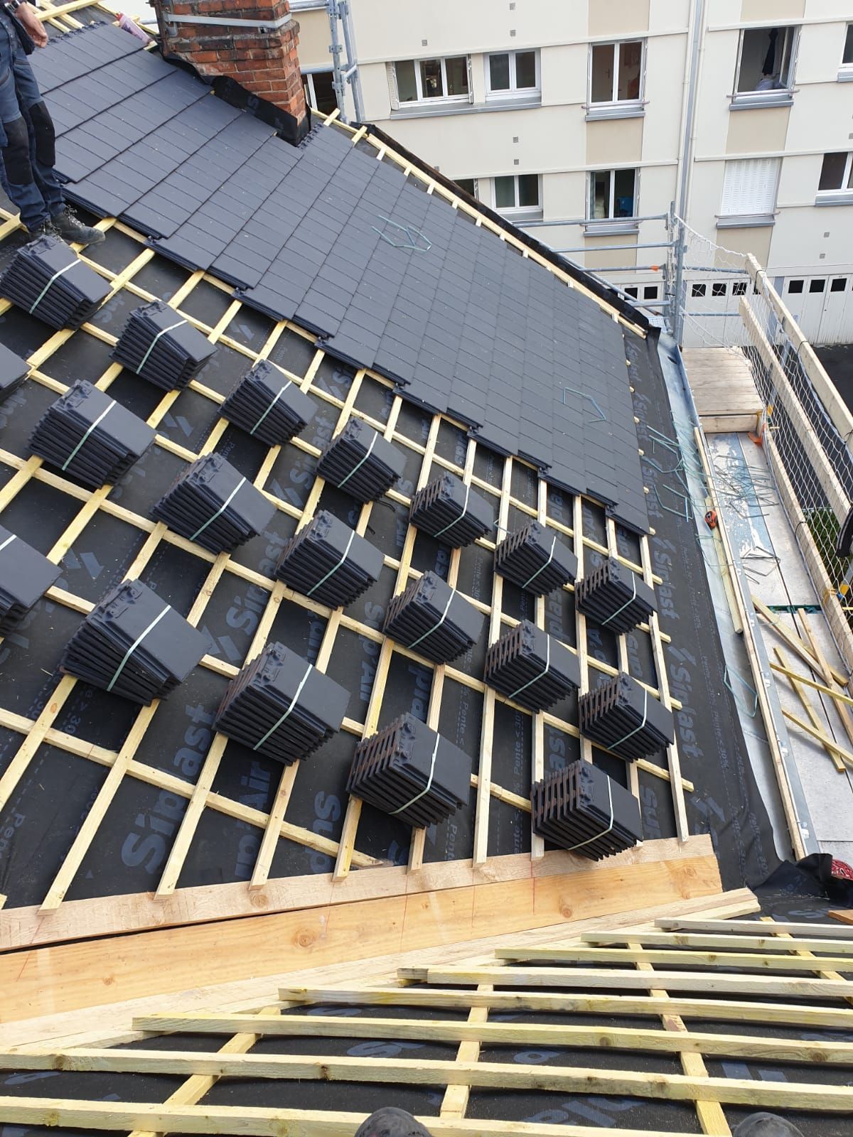Toiture en construction avec panneaux solaires noirs et liteaux jaunes sur un toit en pente.