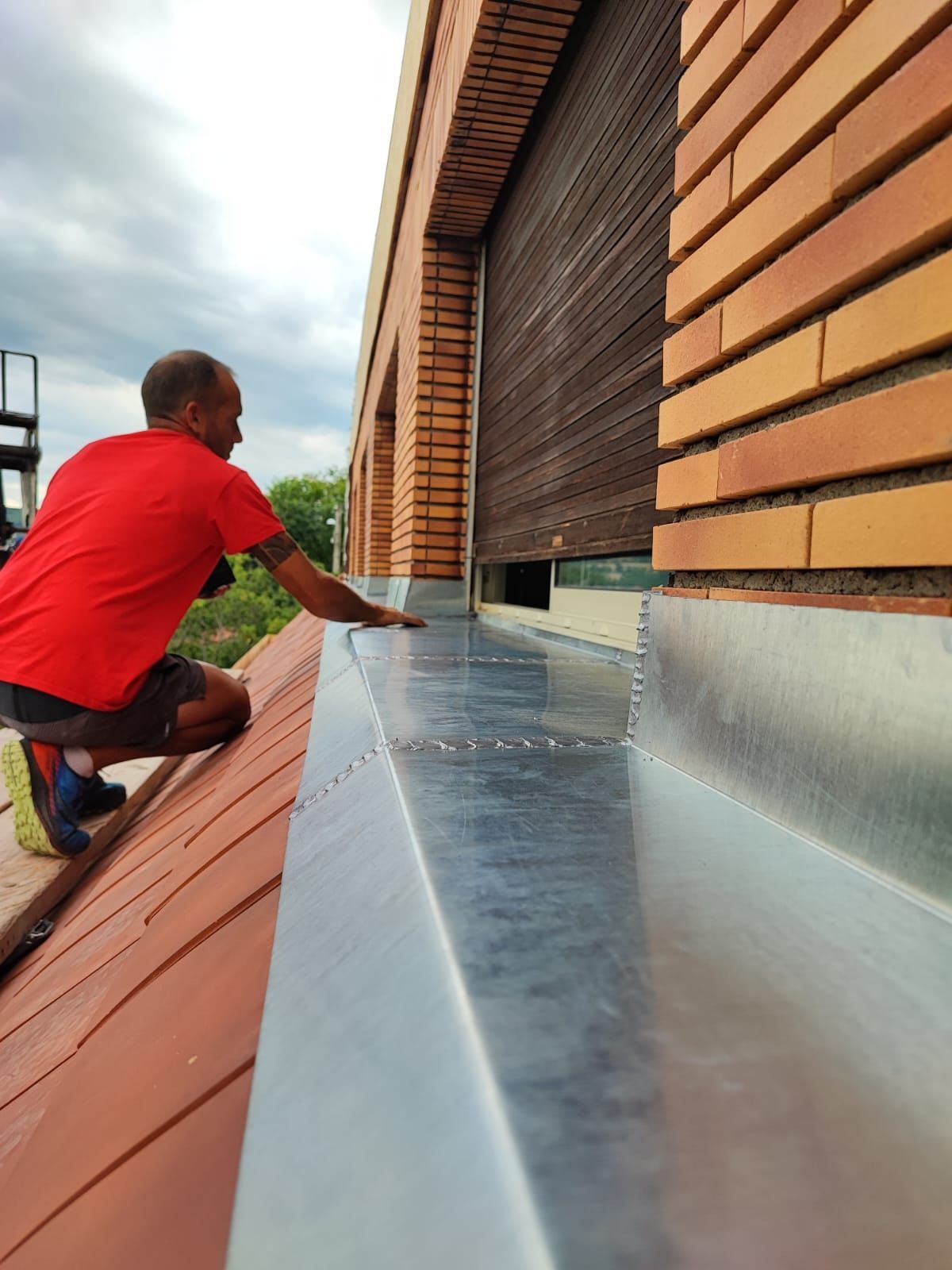 Ouvrier installant une toiture métallique le long d'un mur de bâtiment.