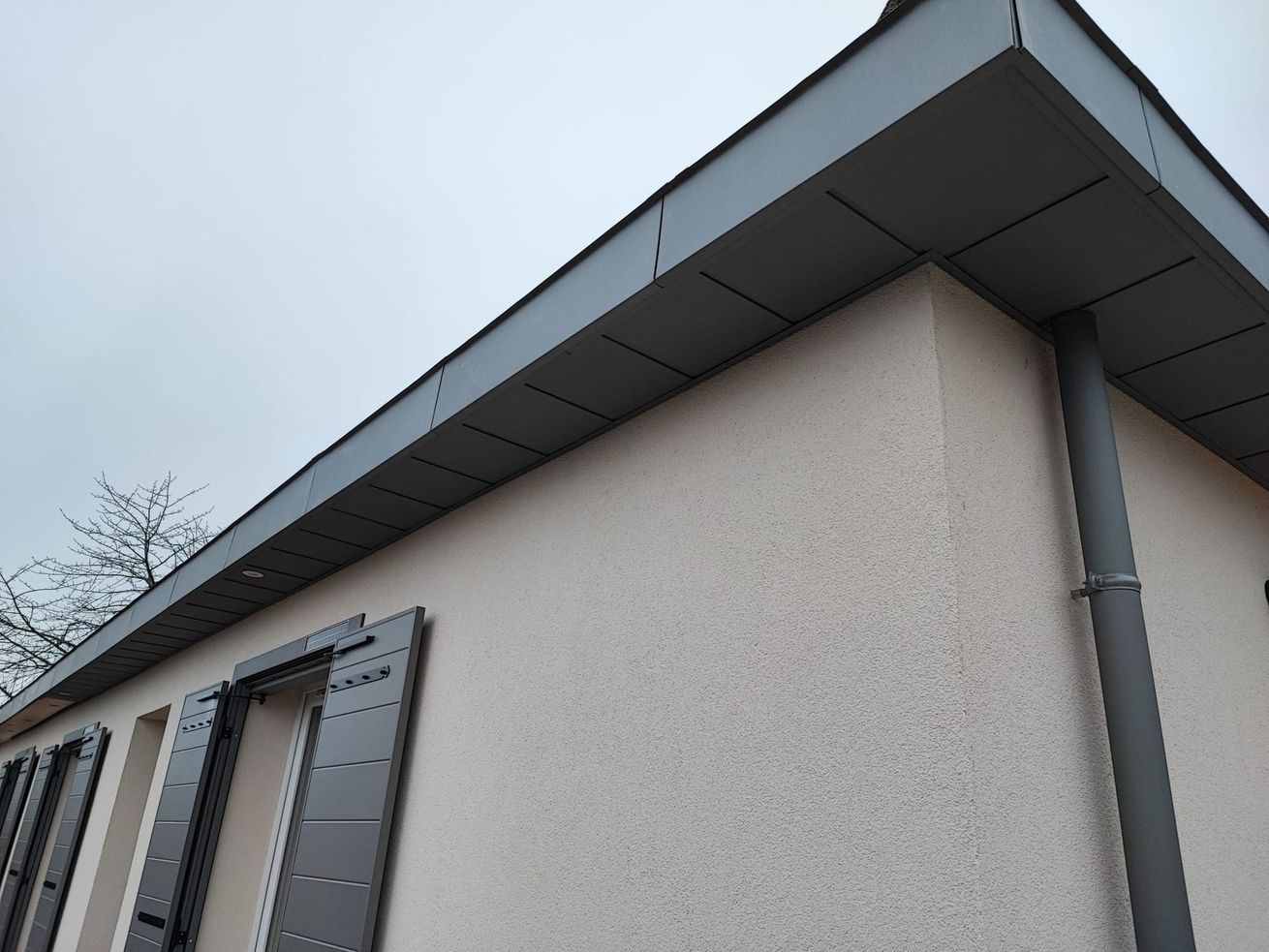 Vue en contre-plongée d'un bâtiment beige avec des ornements de toit gris et des fenêtres à volets.