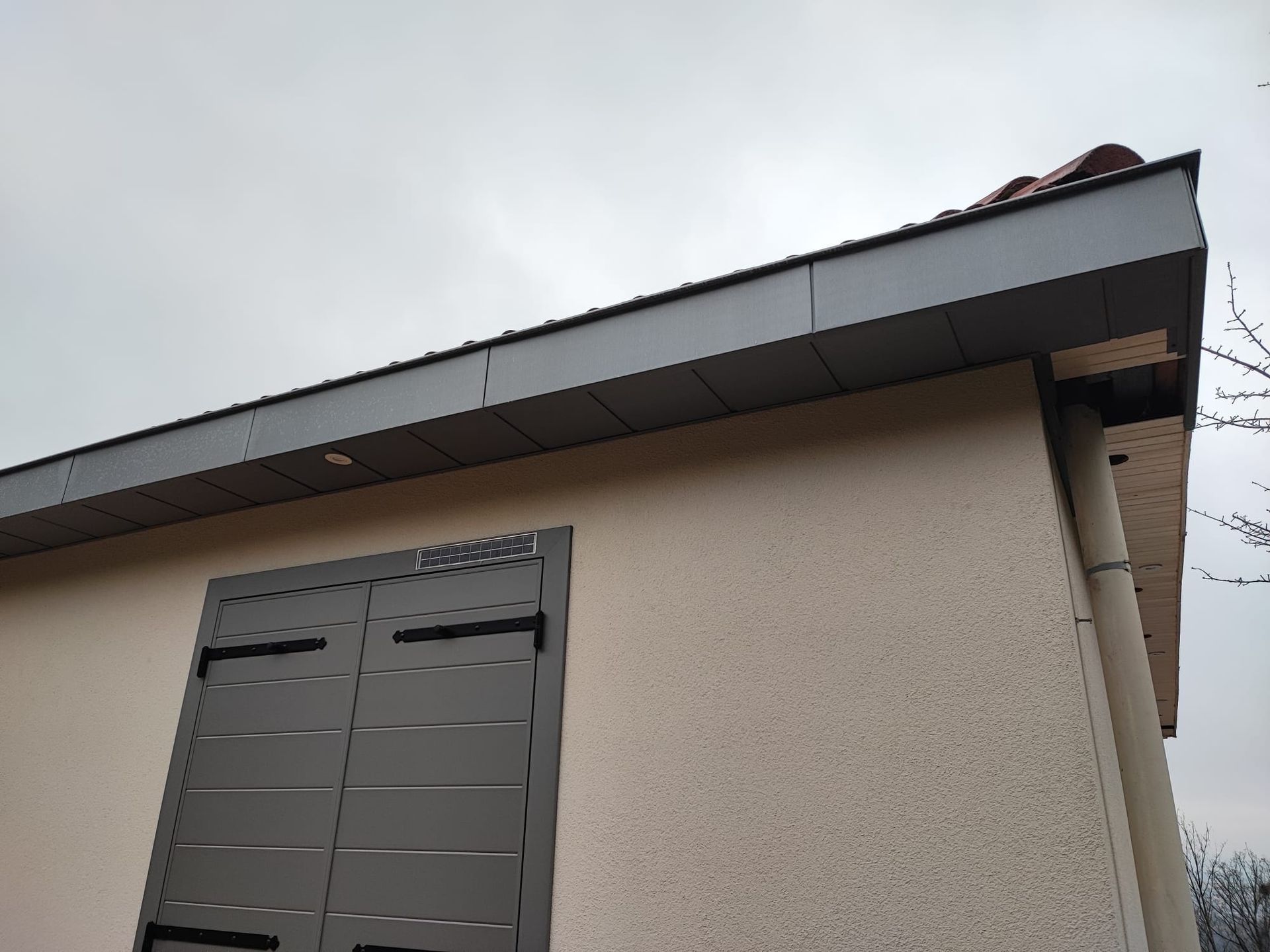 Angle extérieur d'un bâtiment beige au toit gris foncé et à la porte métallique fermée.