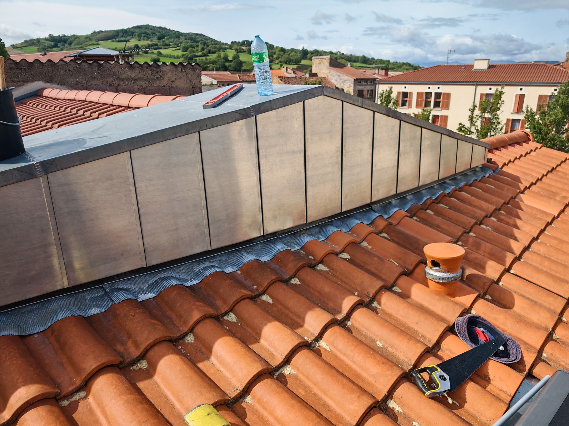 Installation de zinguerie sur un toit de tuiles rouges.
