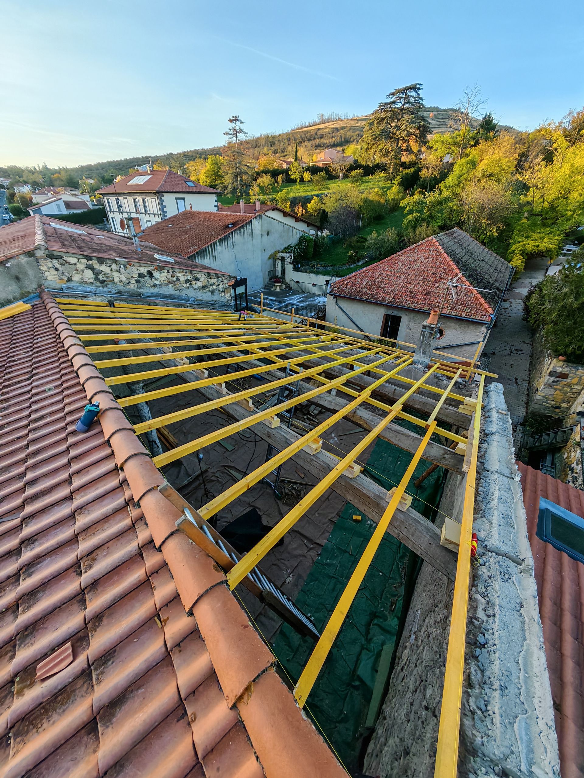 Toiture en réparation avec poutres jaunes et tuiles rouges donnant sur les maisons.