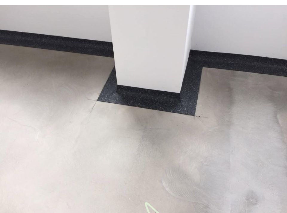 Grauer Betonboden mit einem schwarzen Quadrat um eine weisse Säule.