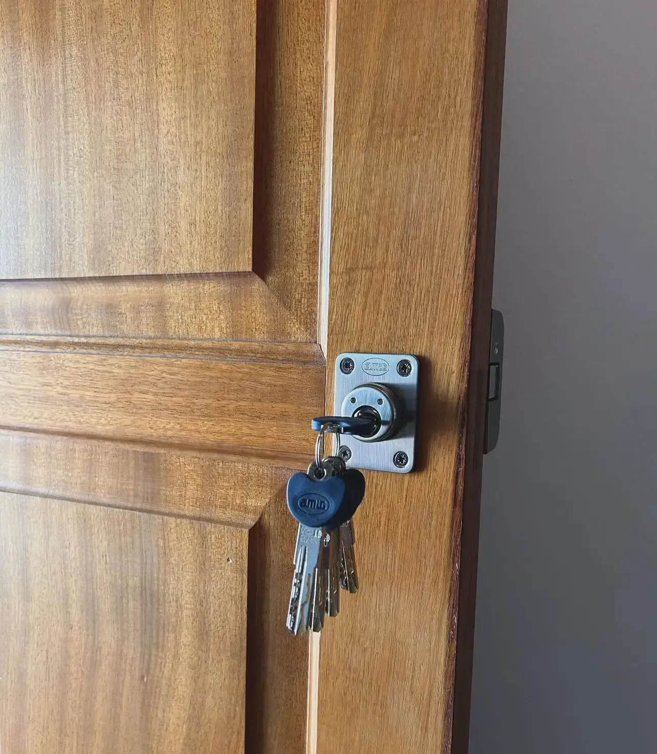 Puerta de madera con llave en la cerradura, acompañada de un llavero de llaves.