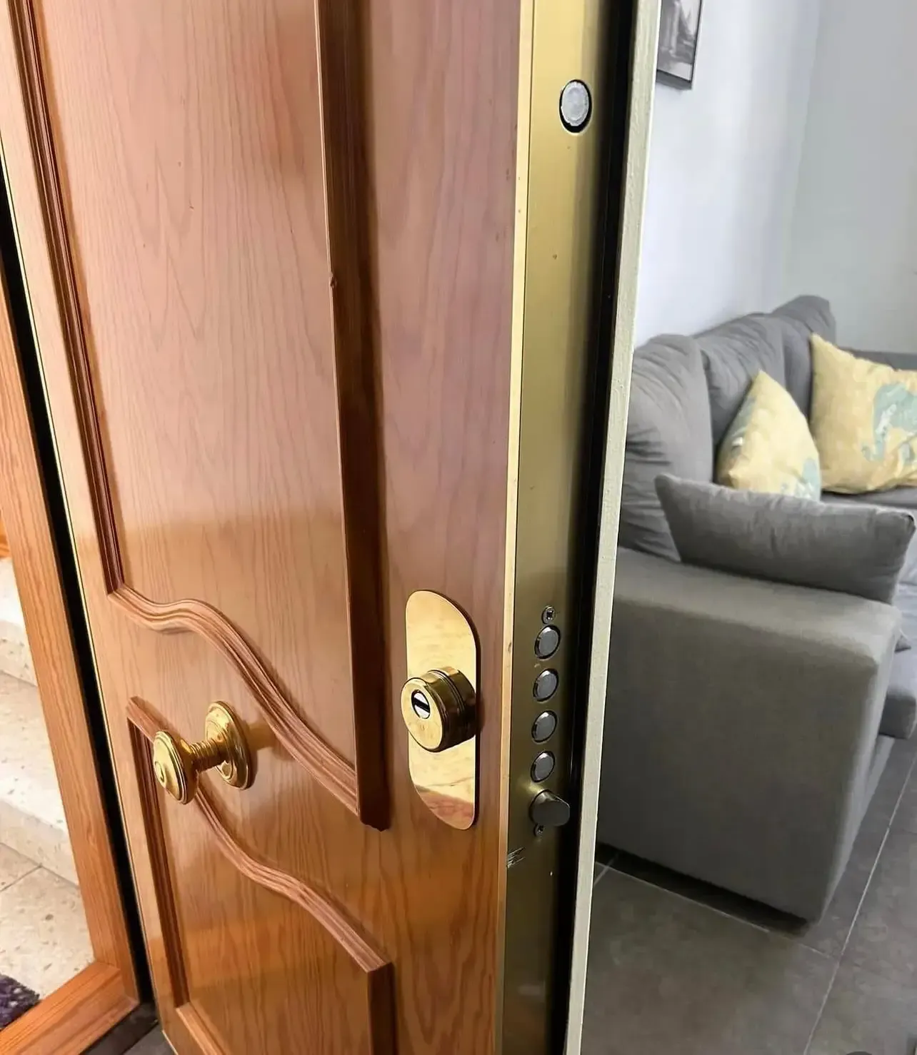 Puerta de madera ligeramente entreabierta, revelando un sofá gris en una sala de estar.