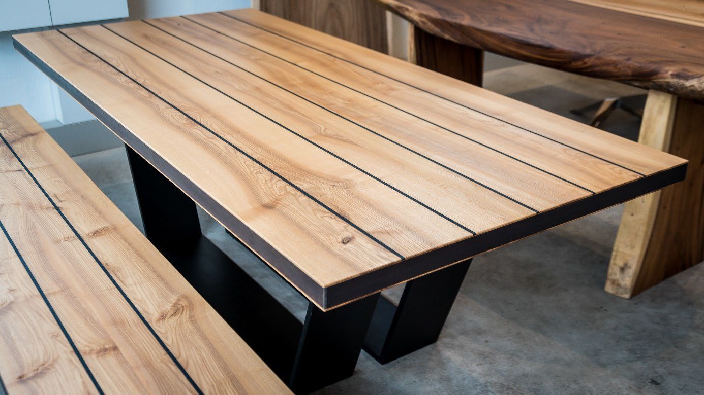 Moderner Holztisch mit schwarzem Metallgestell und passender Holzbank auf Betonboden.