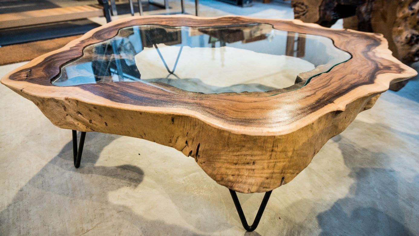 Tisch mit unregelmäßig geformter Holzplatte, deren Mitte mit klarem Harz ausgegossen ist, auf schwarzen Metallbeinen.