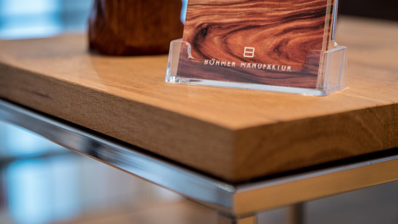 Nahaufnahme einer Holzplatte mit Metallkante und einem transparenten Ständer