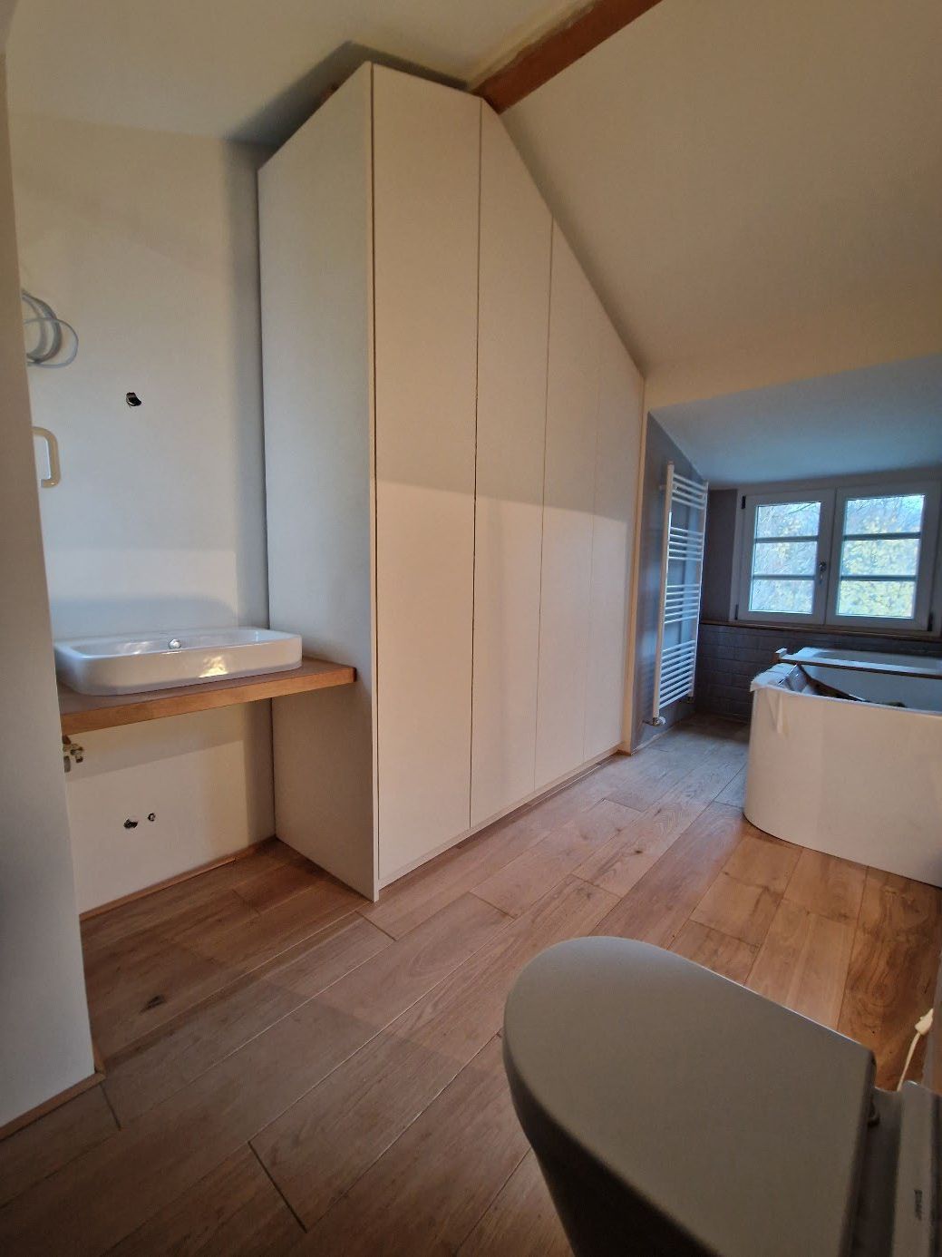 Badezimmer mit eingebautem, schräg zulaufendem Hochschrank, freistehendem Waschbecken auf Holzablage und Badewanne