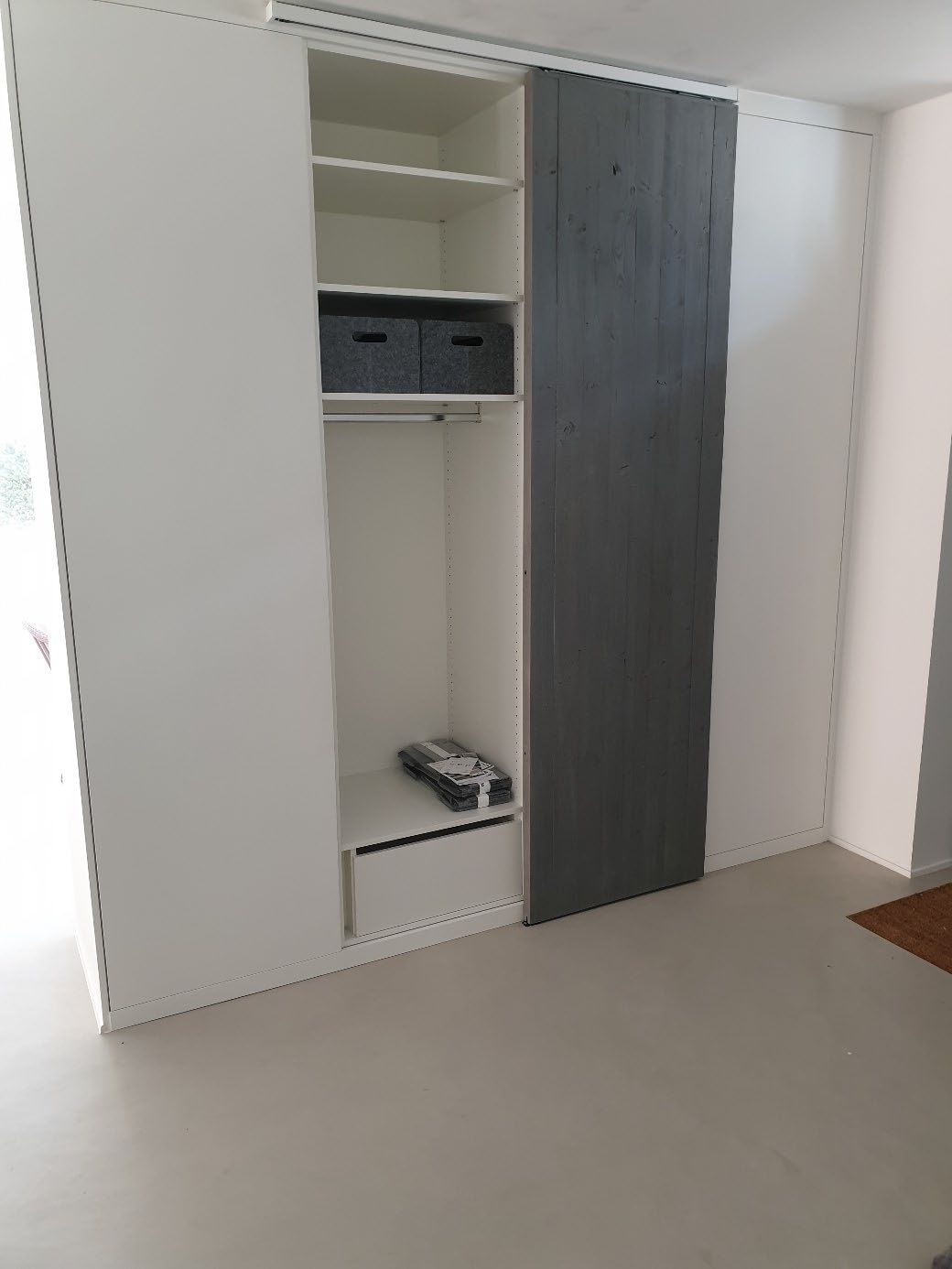 Weißer Einbauschrank mit offenem Fach, zwei grauen Aufbewahrungsboxen und einer grauen Schiebetür.