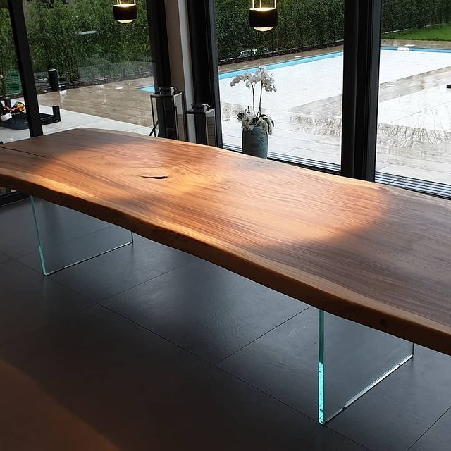 Großer, natürlicher Holztisch mit unregelmäßiger Kante und Glasbeinen vor bodentiefen Fenstern