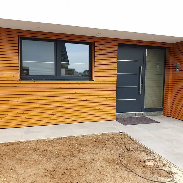 Moderne Holzfassade mit Fenster und dunkler Eingangstür.