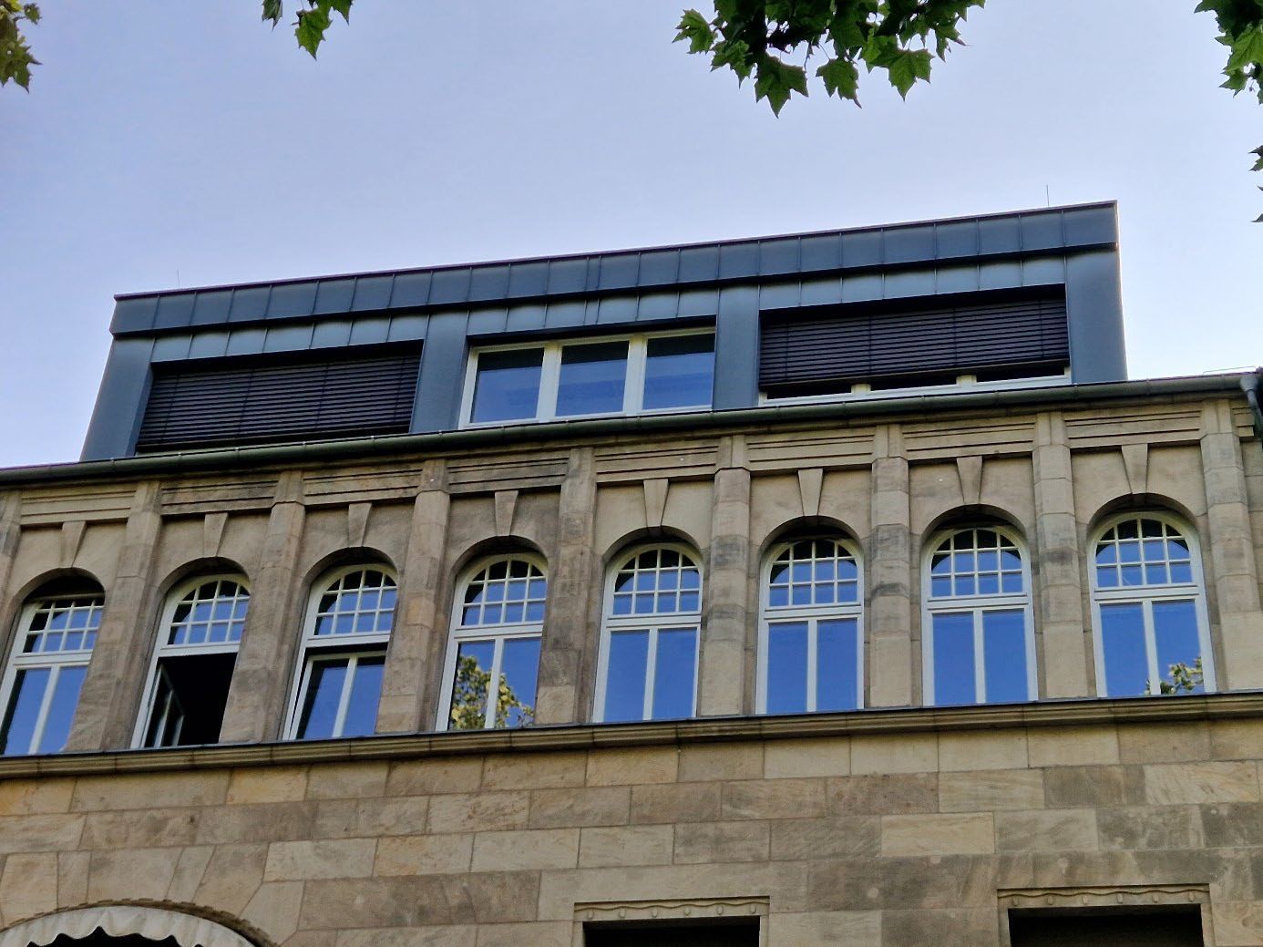 Historisches Gebäude mit moderner Holzfassade im oberen Bereich.