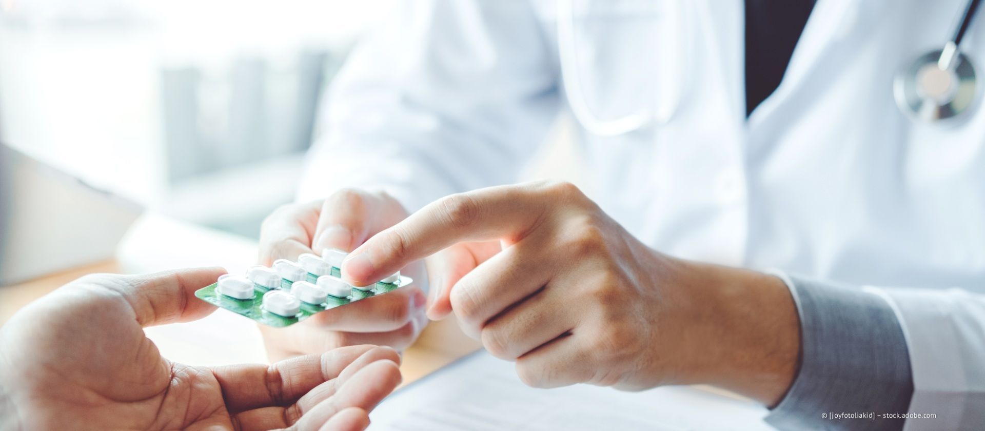 Ein Arzt zeigt auf Tabletten in einer Blisterpackung und reicht sie einem Patienten.