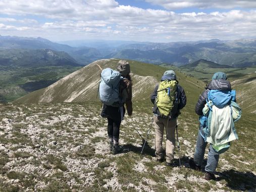 Trois enfants en tenu de randonnée se tenant devant un paysage de montagne.