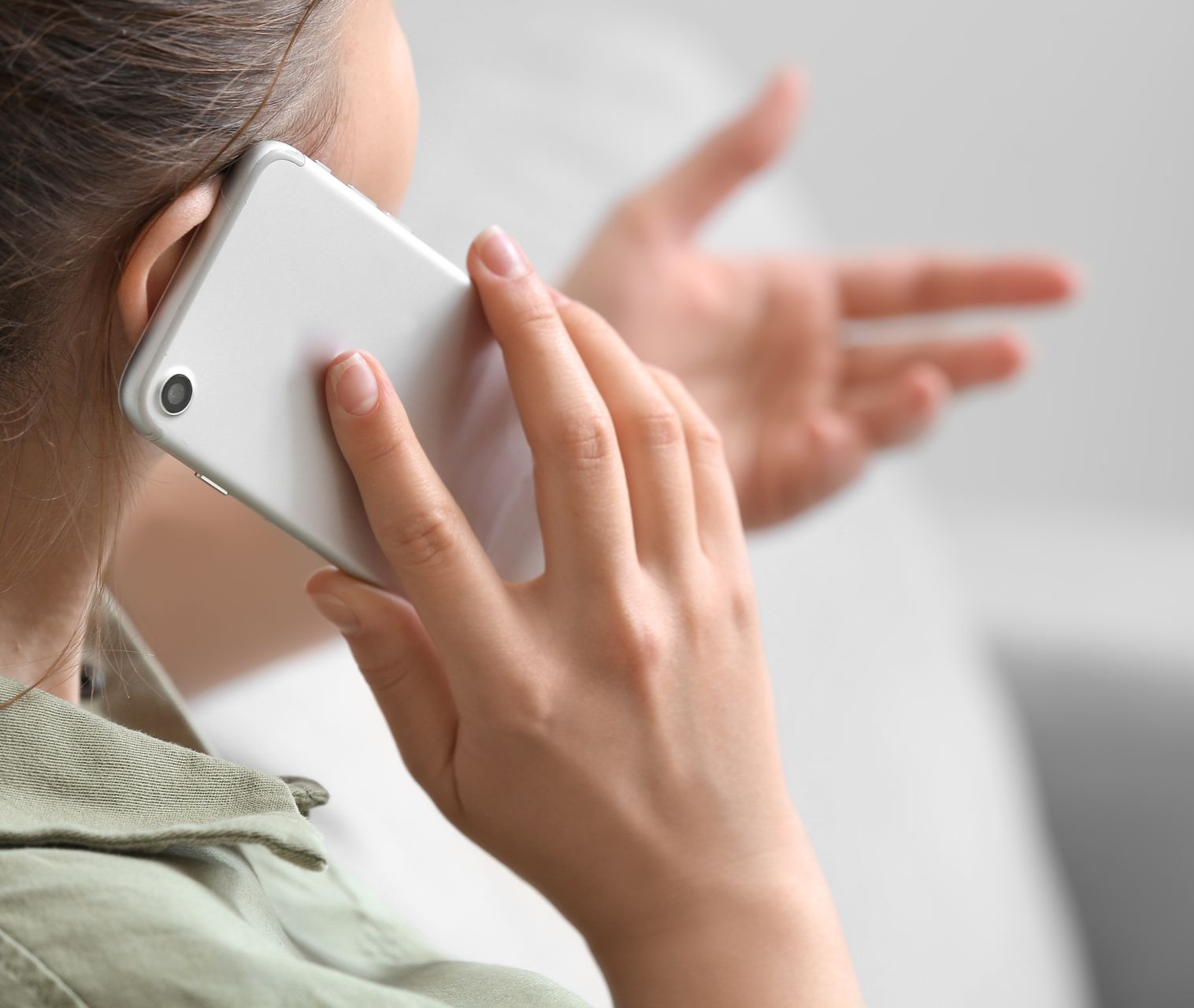 Une personne tenant un smartphone blanc à l'oreille tout en parlant et en gesticulant de l'autre main