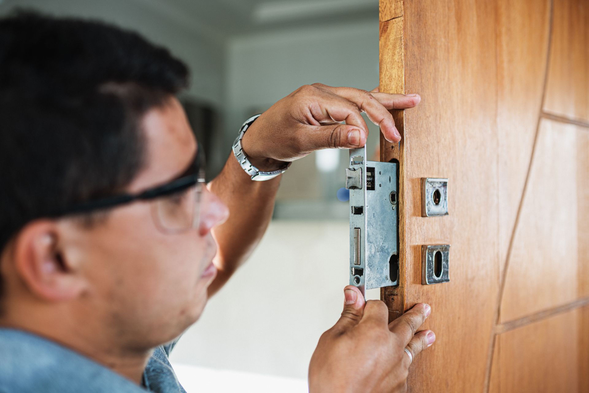 Une personne installe une serrure métallique sur une porte en bois à l'aide d'un tournevis.