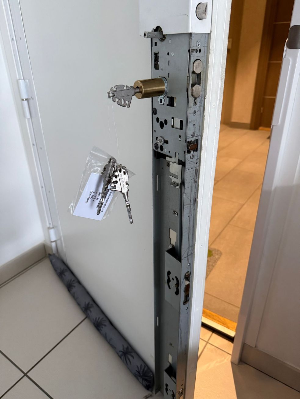 Serrure de porte cassée avec porte-clés pendant sur une porte blanche entrouverte dans un couloir carrelé