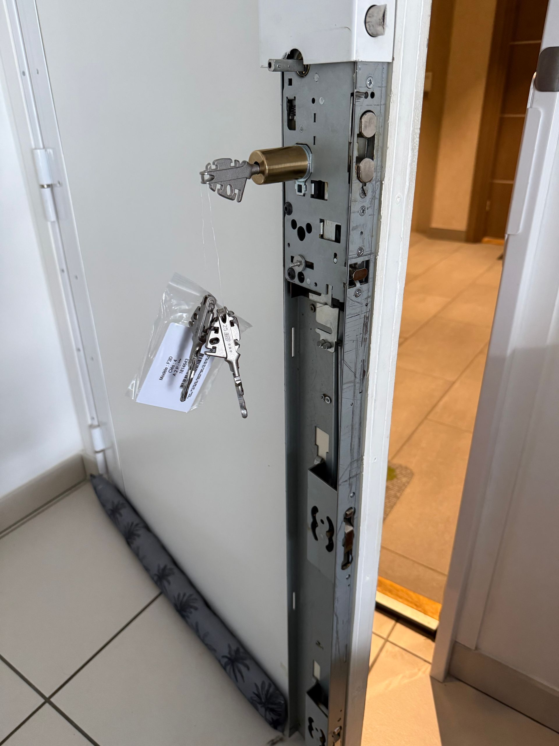 Porte blanche entrouverte avec serrure cassée et porte-clés accroché dans un couloir carrelé