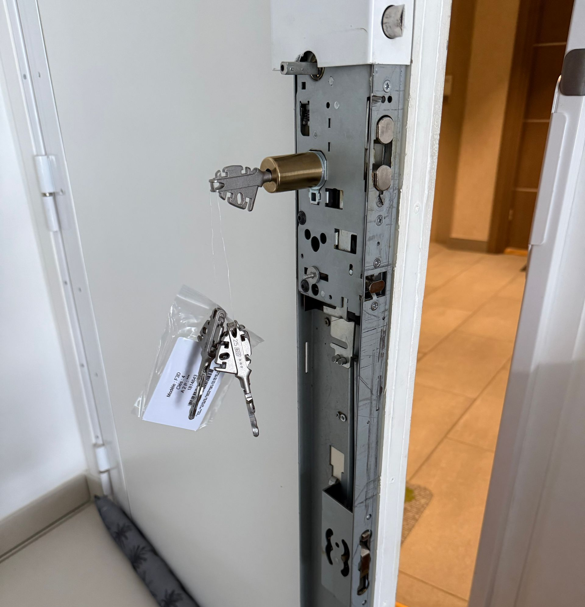 Porte blanche ouverte dans un couloir, serrure endommagée et porte-clés suspendu