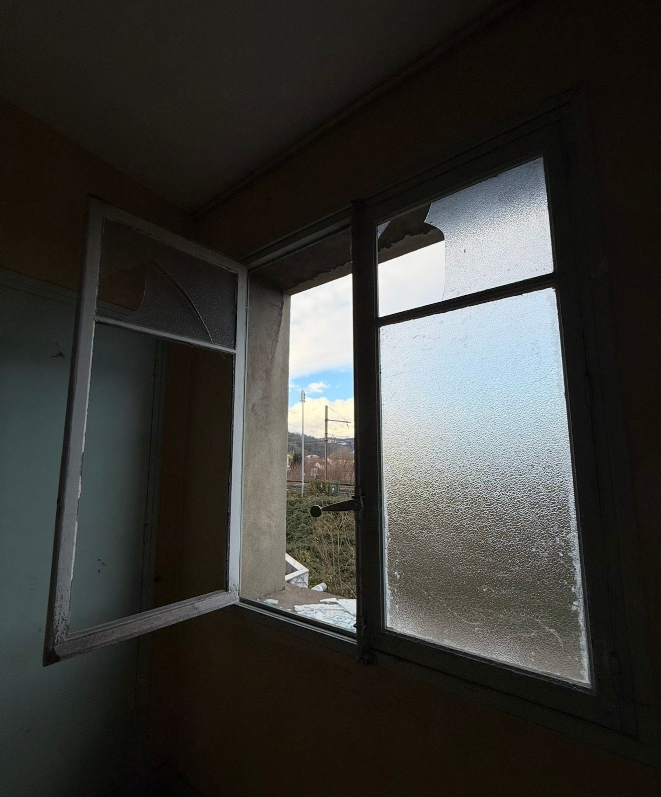 Fenêtre ouverte aux vitres dépolies donnant sur un ciel nuageux et des bâtiments