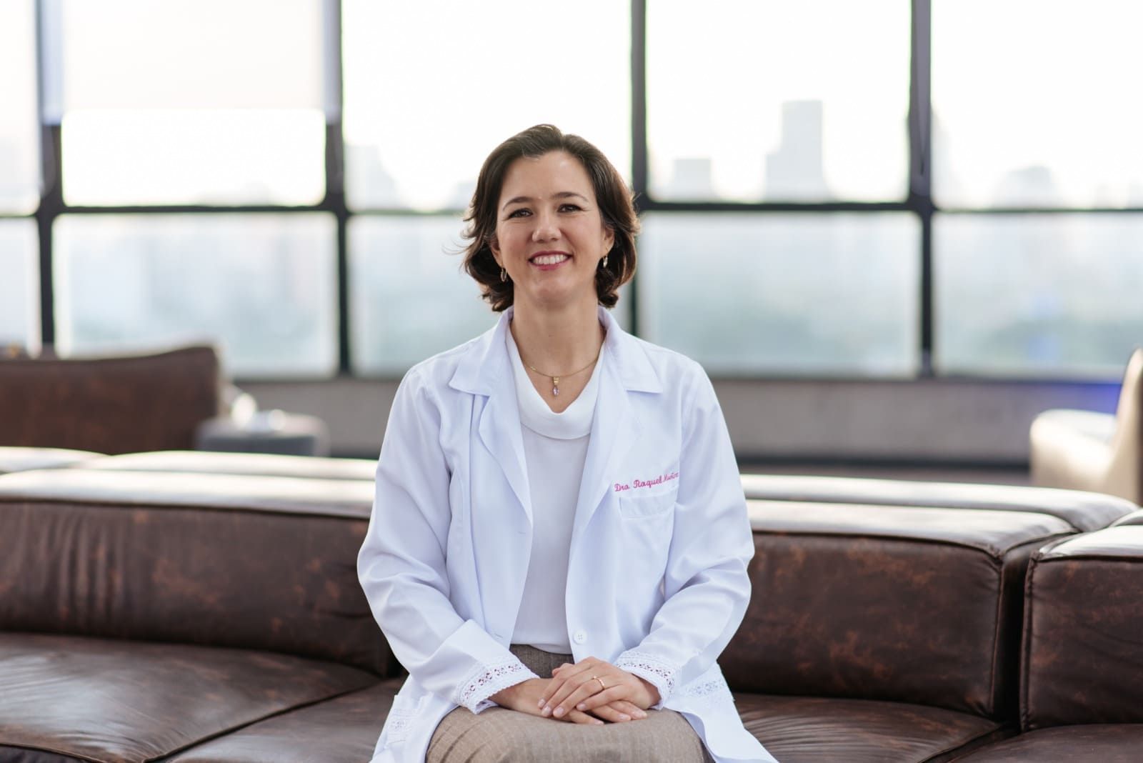 Una mujer con una bata de laboratorio blanca está sentada en un sofá.
