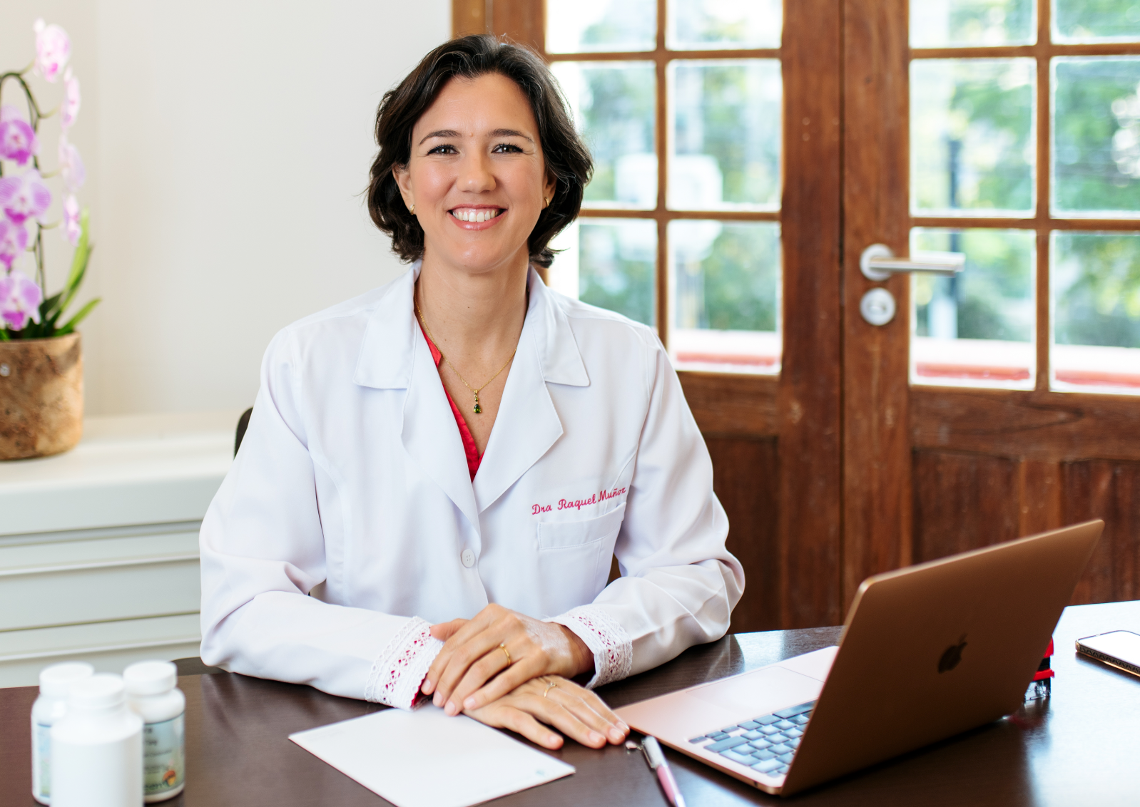 Una mujer con una bata de laboratorio está sentada en un escritorio con una computadora portátil.