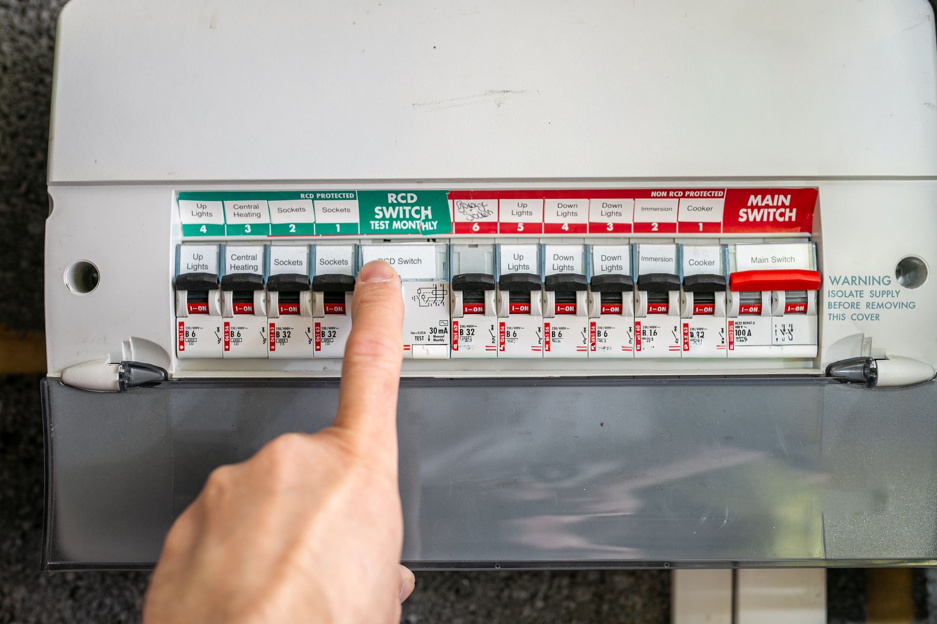 Un doigt pointant vers une rangée de disjoncteurs dans un tableau électrique.