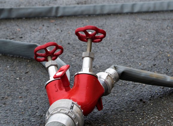 Vannes de borne d’incendie reliées à un tuyau posé sur le trottoir.