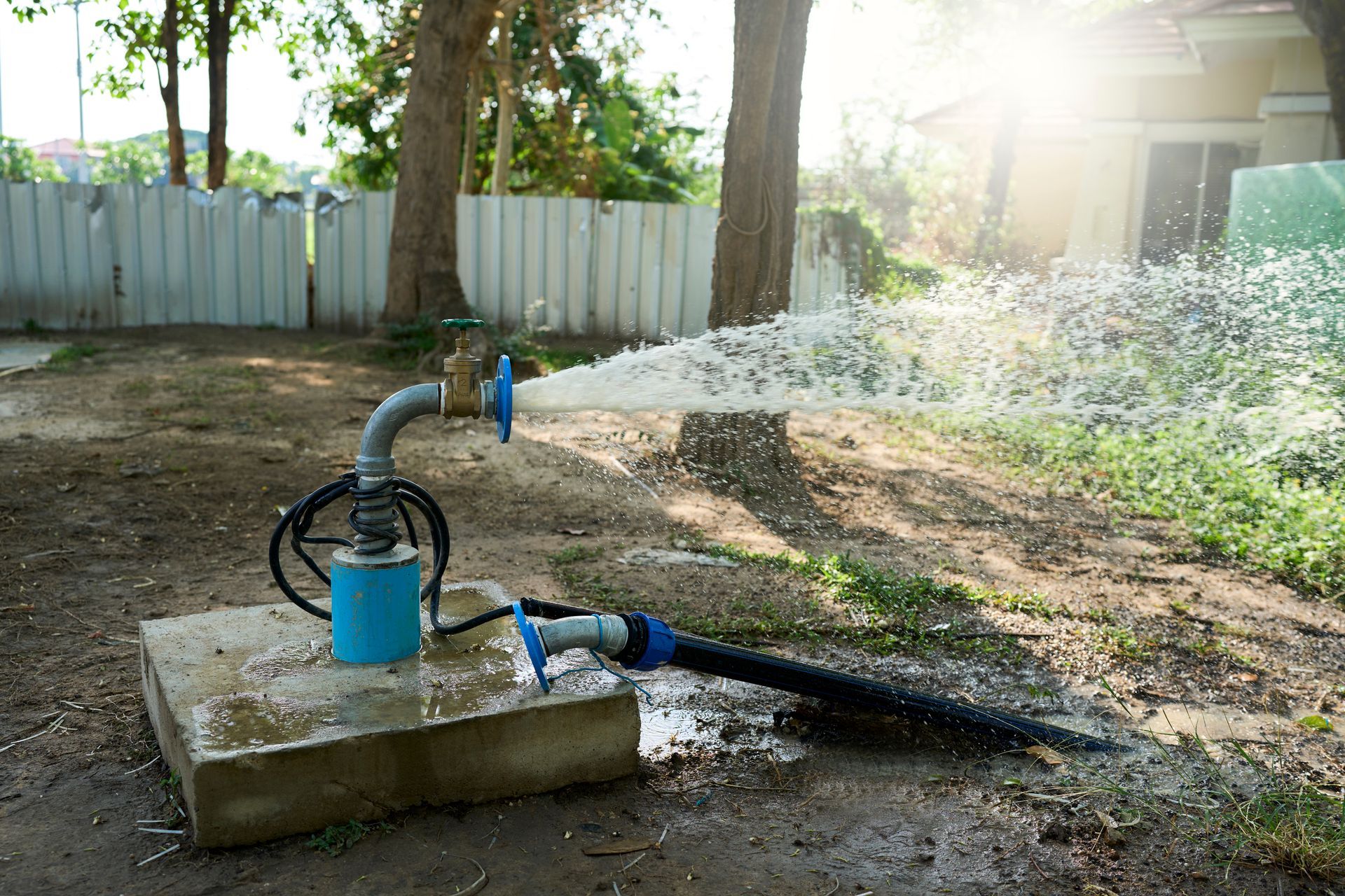 Une pompe à eau projette de l’eau sur le sol dans une cour.