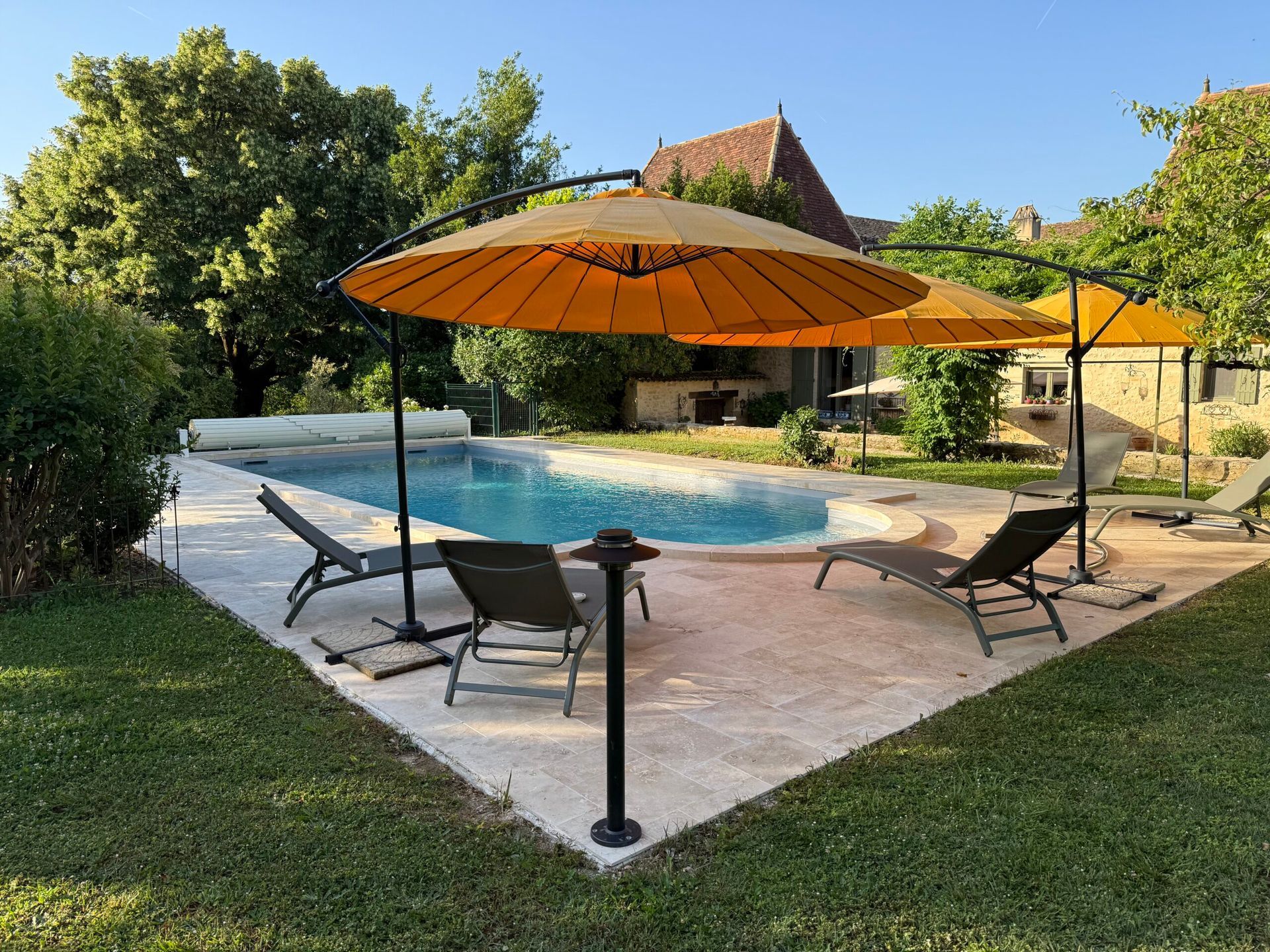 Piscine dans le jardin avec des chaises longues et un parasol orange, à côté d’une terrasse en pierre