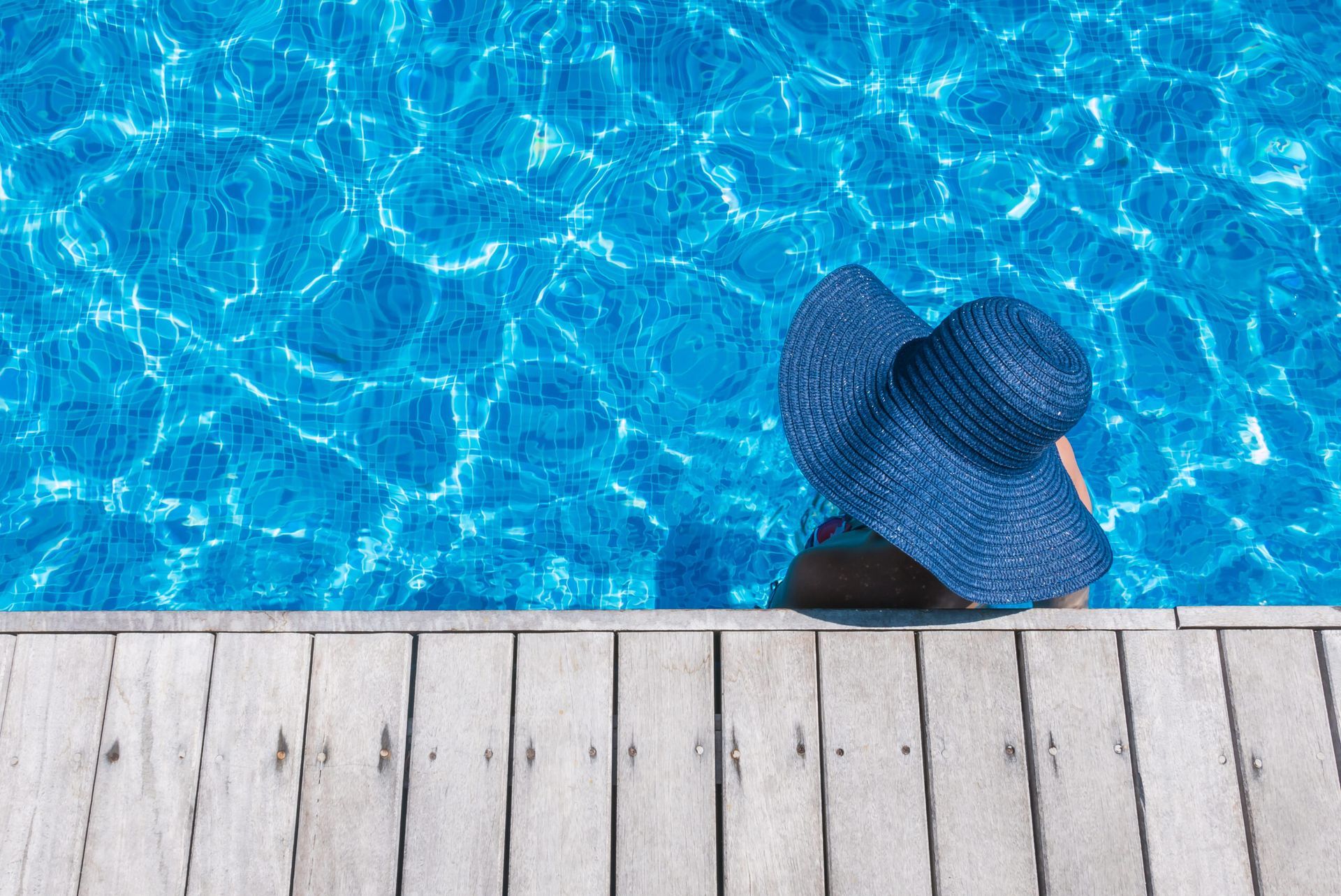 Chapeau de soleil bleu flottant dans une piscine ensoleillée, près d’une terrasse en bois