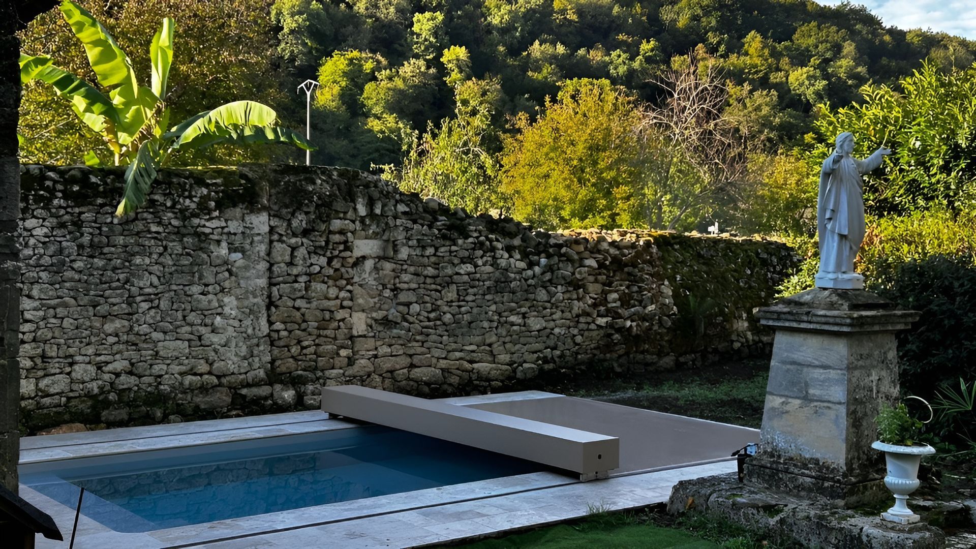 Cour intérieure entourée de murs en pierre, avec une petite piscine, une terrasse en bois et une statue blanche