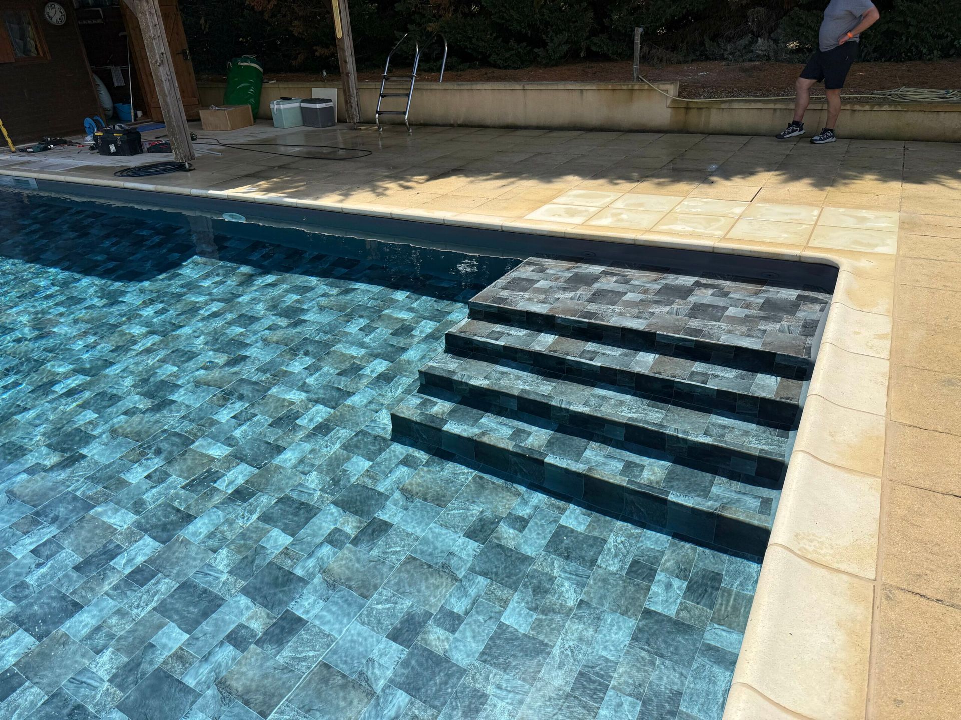 Piscine avec des carreaux bleus, des marches et une plage beige à côté