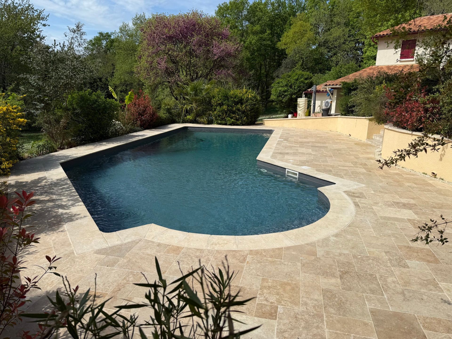 Piscine de jardin aux formes arrondies, bordée d’une terrasse en pierre et d’une végétation luxuriante