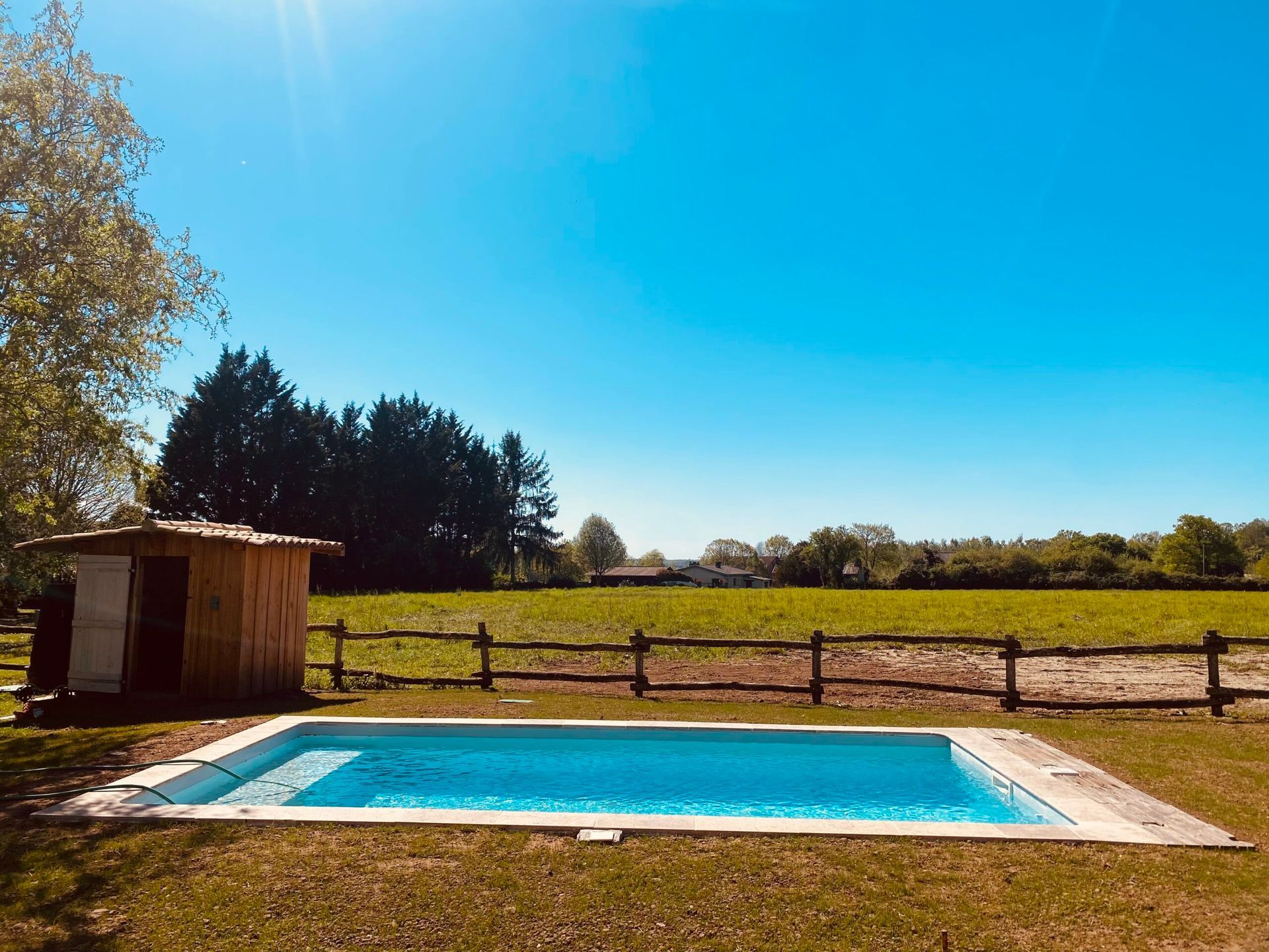 Piscine dans le jardin, près d’un petit abri, avec un champ dégagé et un ciel bleu en arrière-plan