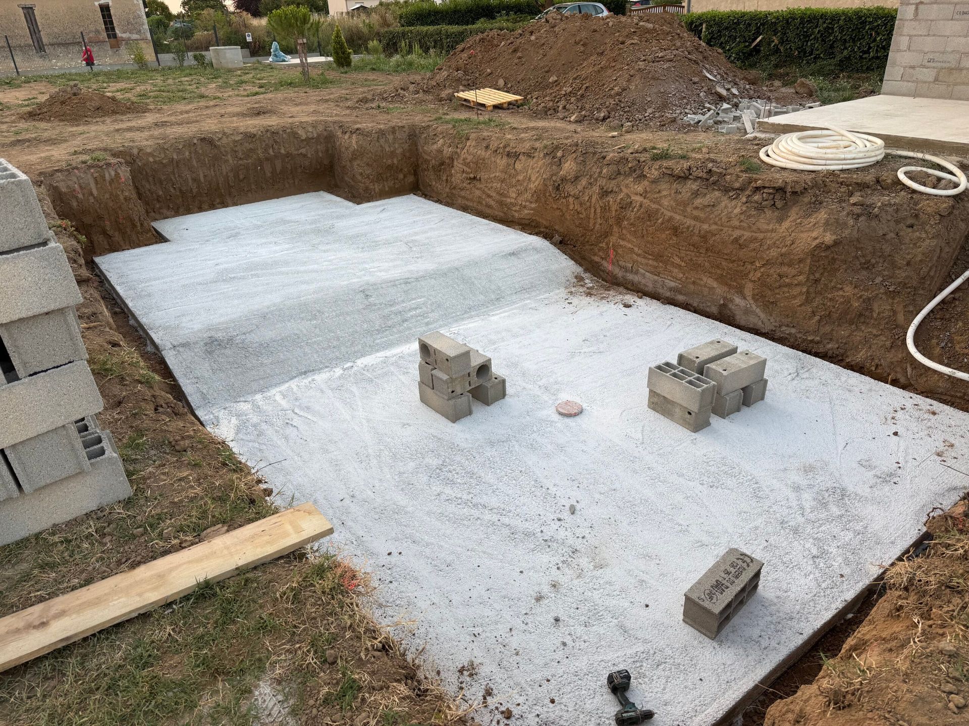 Excavation des fondations avec un lit de gravier blanc, des parpaings empilés et des parois en terre sur un chantier
