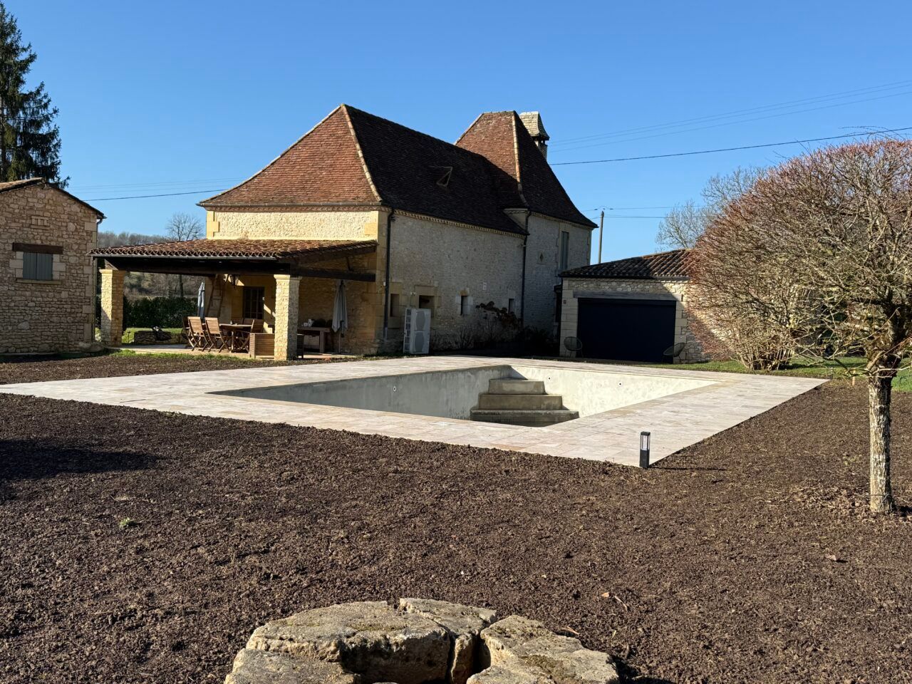 Cour intérieure avec une maison en pierre, un toit de tuiles rouges, une piscine pavée et un arbre taillé