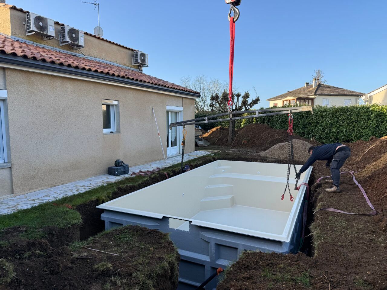 Arrière-cour où une grande piscine blanche est descendue à l’aide d’une grue dans une fosse creusée à cet effet