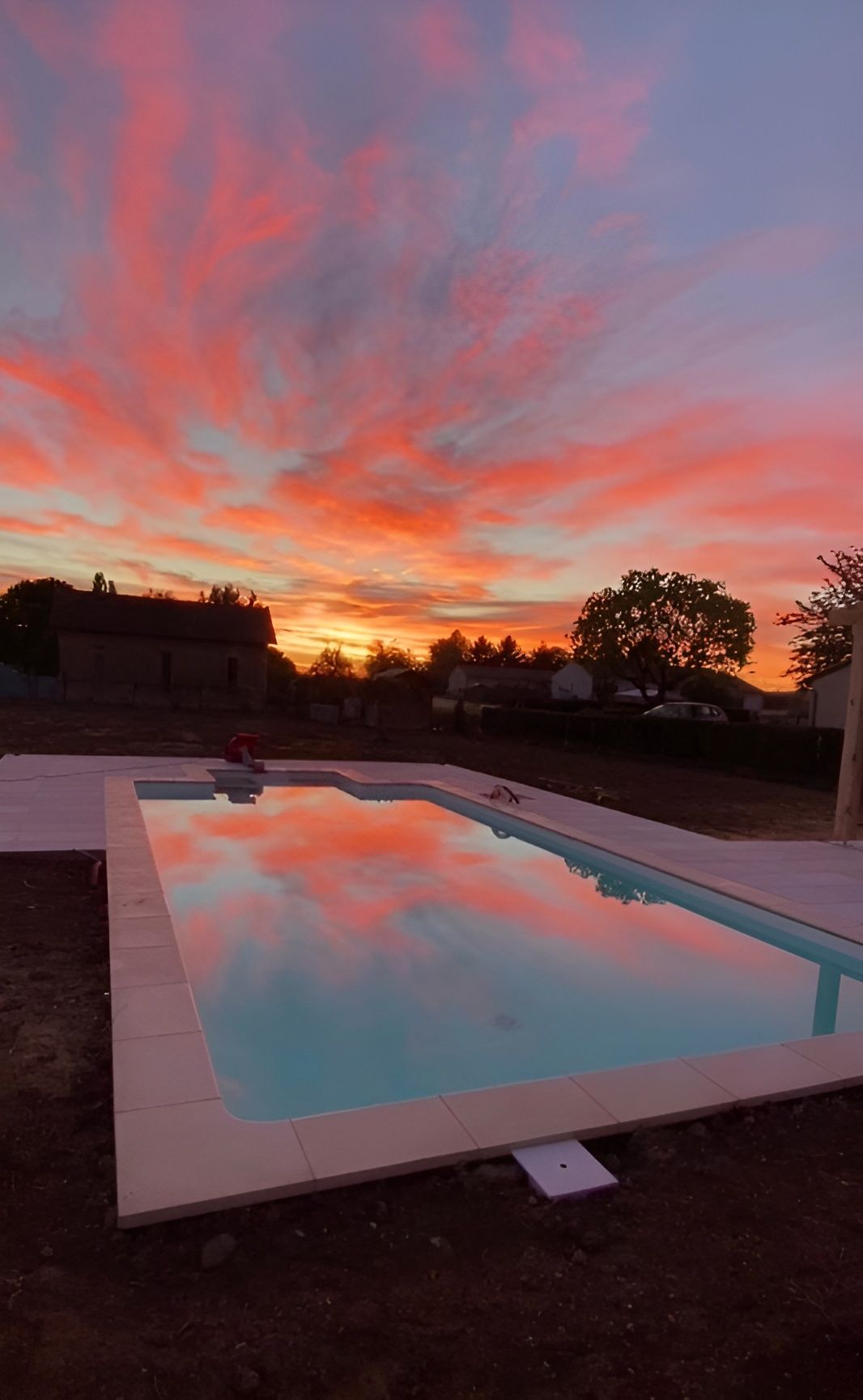 Piscine rectangulaire reflétant un coucher de soleil éclatant aux teintes rose et orange, avec des nuages