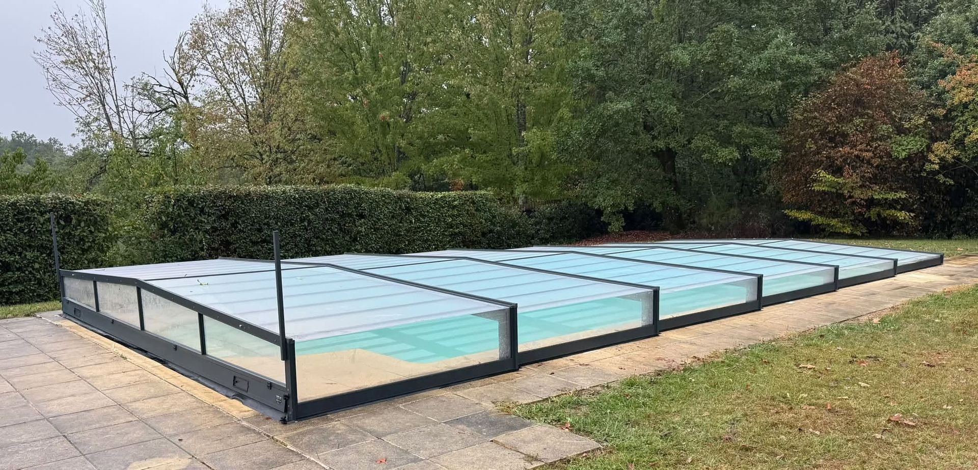 Piscine rectangulaire extérieure à l’eau bleu clair, entourée d’une structure en métal noir et d’une terrasse pavée