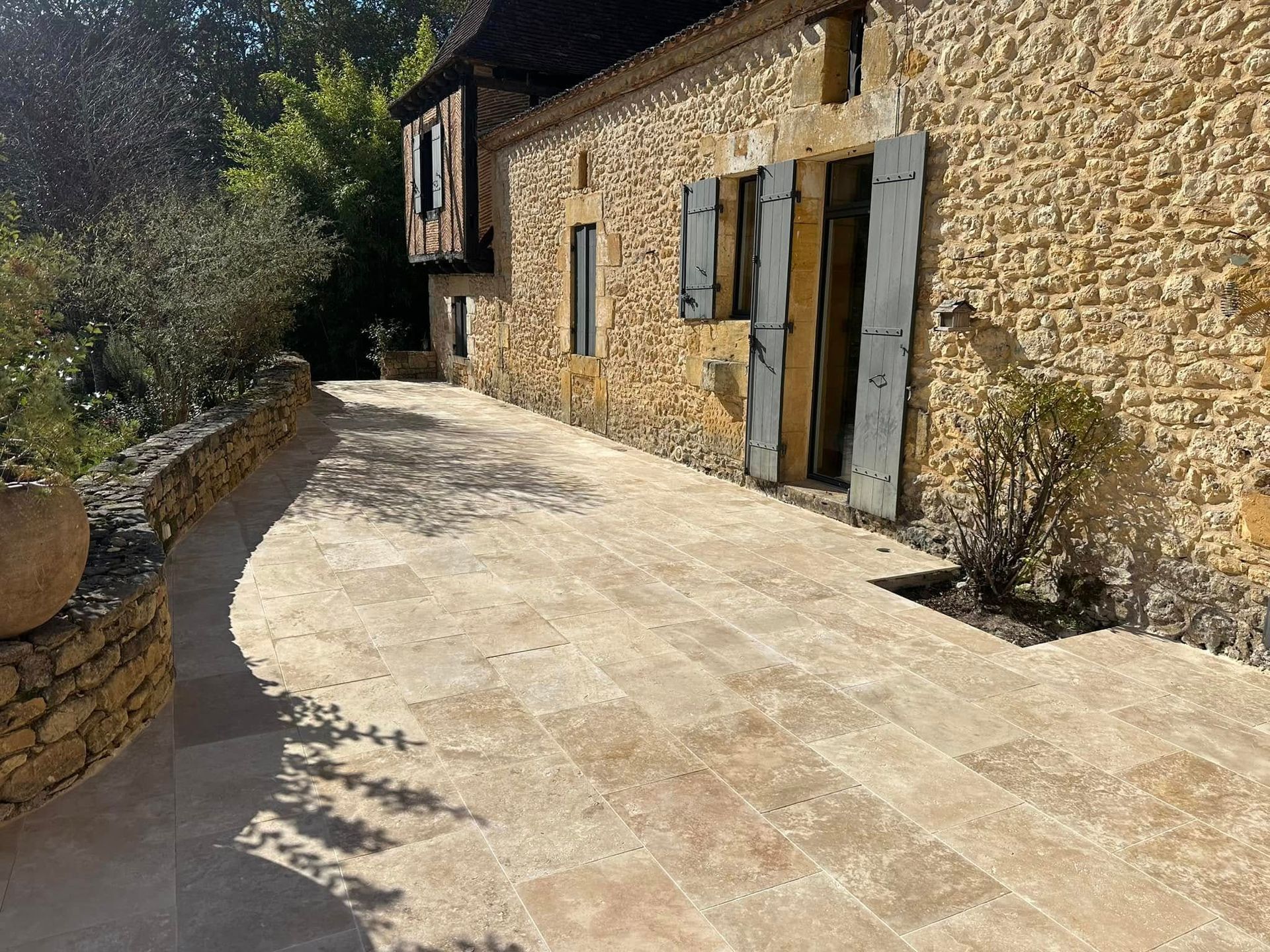 Maison en pierre aux fenêtres à volets et chemin pavé dans une cour ensoleillée