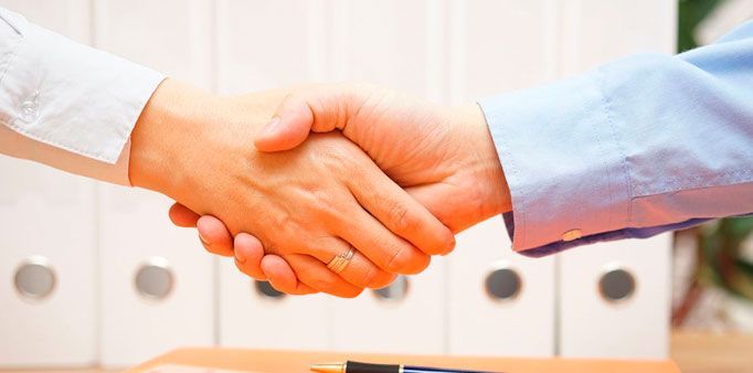 Dos personas se dan la mano sobre una mesa.