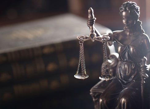 Una estatua de la Dama de la Justicia sosteniendo una balanza de la justicia frente a un libro.