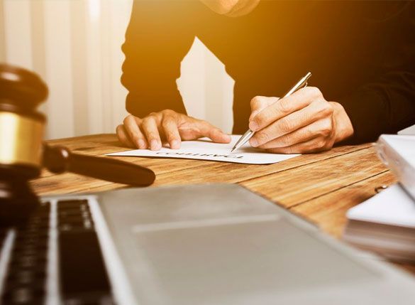 Una persona está sentada en una mesa escribiendo en un trozo de papel.