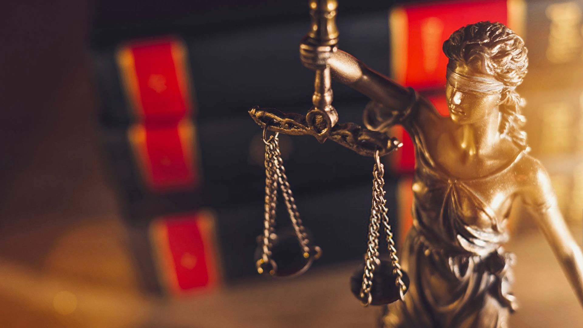 Une statue de dame justice tenant une balance devant une pile de livres.