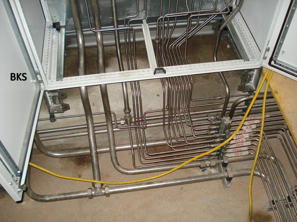 Offener Schrank mit zahlreichen gebogenen Edelstahlrohren und gelben elektrischen Leitungen.